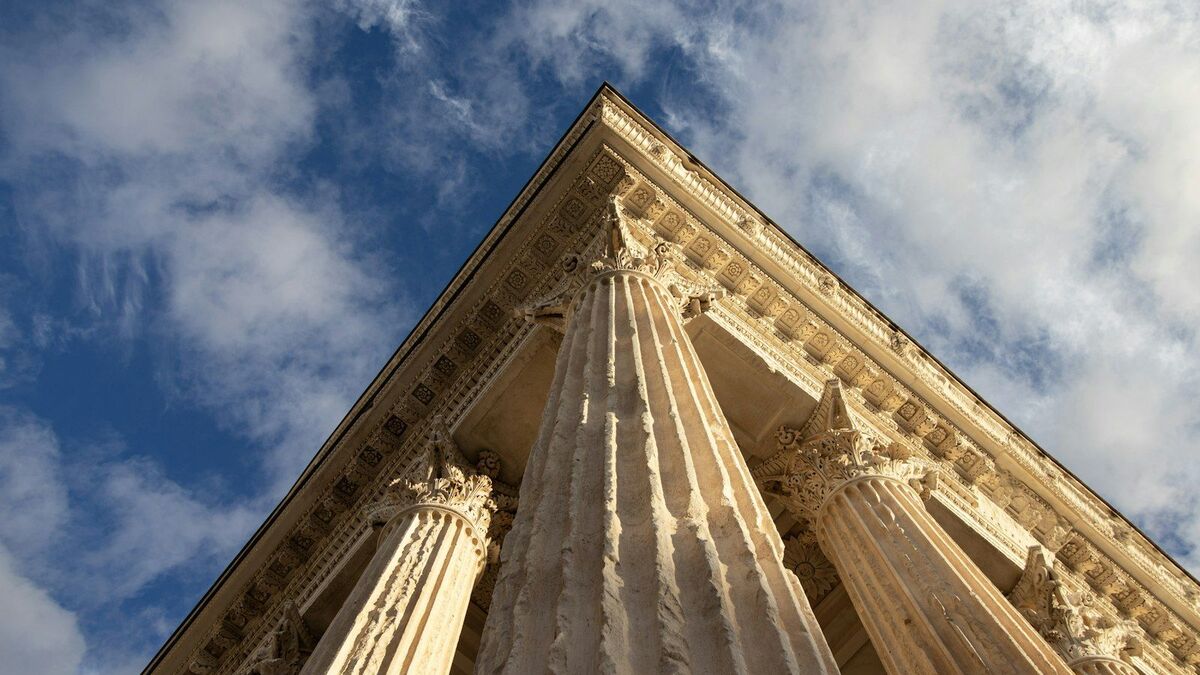 Looking up at the corner of a stone building where two rows of columns intersect against the sky.