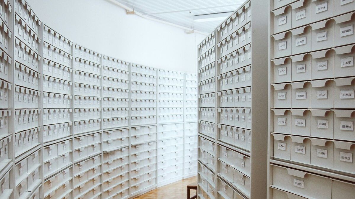 Rows of white labelled archive boxes on shelving in a records room.