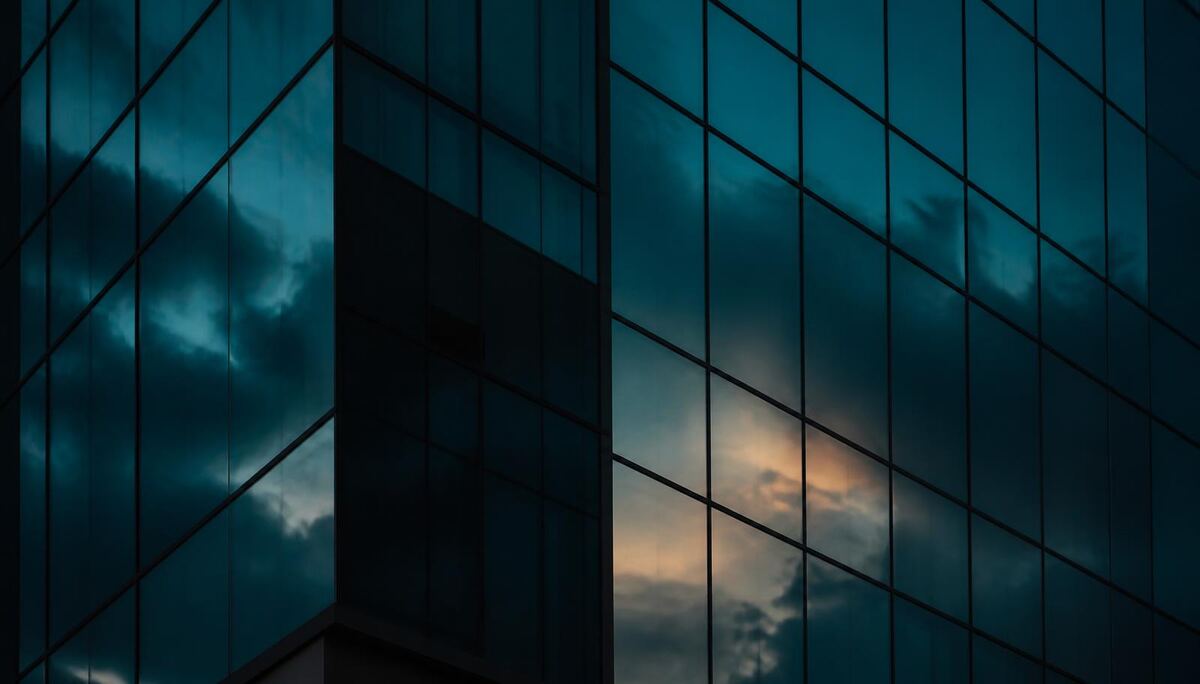 Abstract close-up of a dark glass office facade reflecting a teal dusk sky.