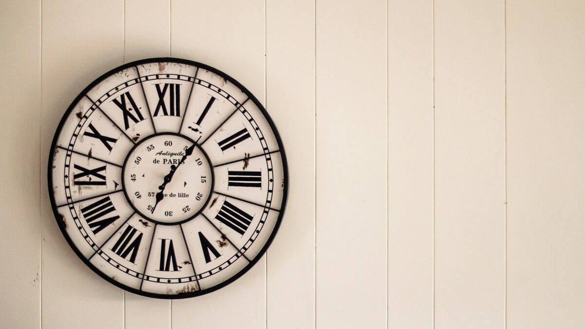 A large Roman-numeral wall clock mounted on a pale panelled interior wall.
