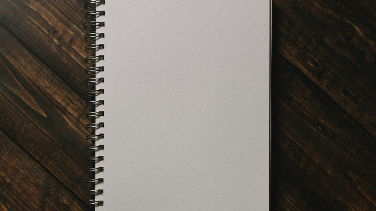 A closed spiral-bound notebook on a dark timber desk.